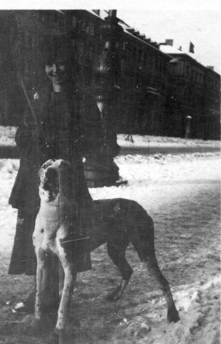 En kvinna med en hund på en stadsgata. Det ligger snö på marken.