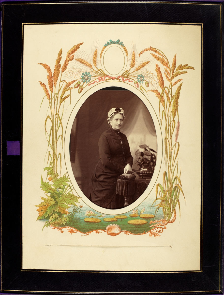 Stående portrett av en eldre dame i mørk kjole og med lys kyse. Dekorert passepartout med botaniske tegninger. 
Portrett av Elsbetha  (Betha) Thorsen (1807-1888) født Heftye, som var tanten til Nini Wedel Jarlsberg (1827-1897) på Bogstad gård.