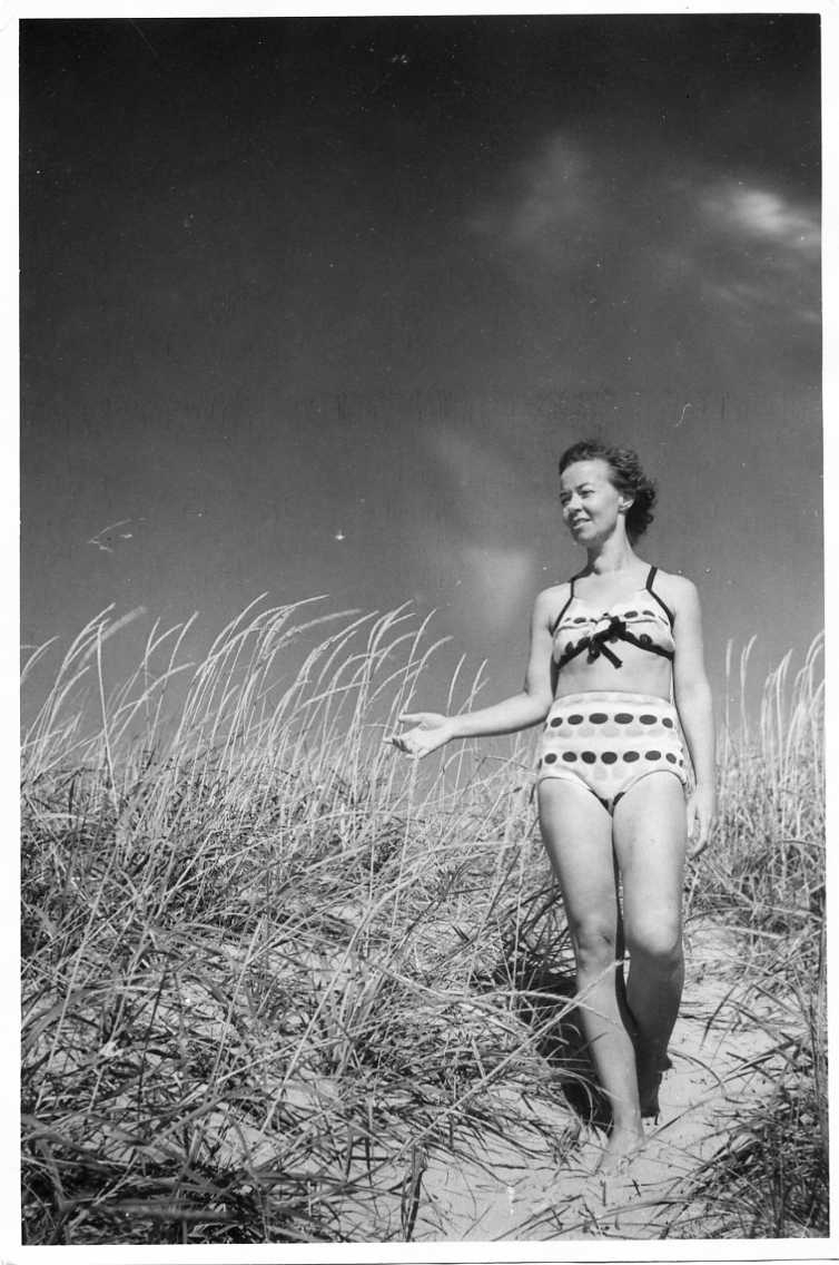 En kvinna i prickig bikini kommer gående nedför en gräsbevuxen sandslänt.