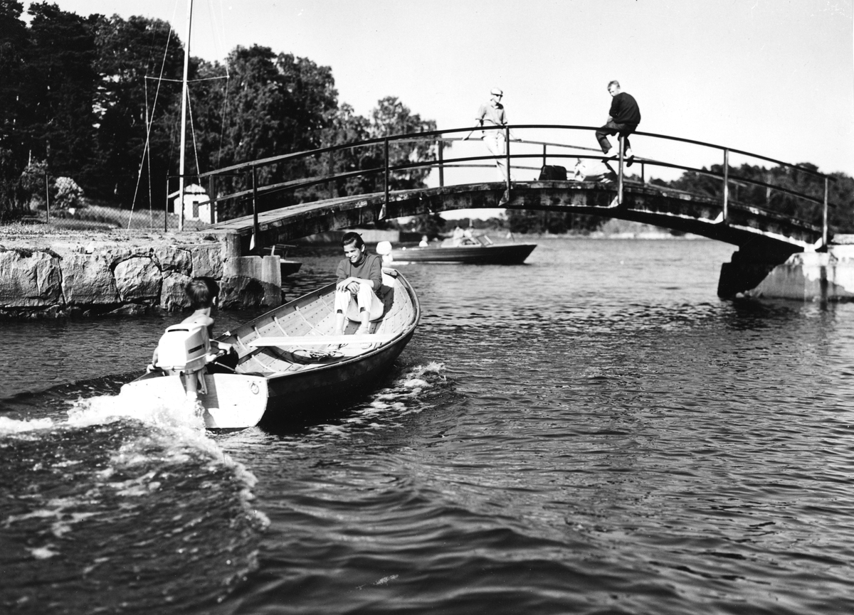 Småbåt med utombordsmotor (Electrolux Penta E4) på väg att passera en mindre bro där två tonårspojkar står.