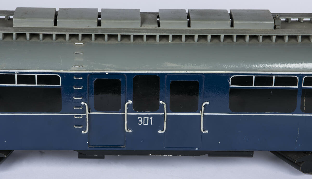 Tremodell i en mørk blå farge, med sorte vinduer og grått tak av forstadsbane fra Bærumsbanen med nr. 301. Modellen har detaljerte utskjæringer og malingsdetaljer som gjør den tro til originalen. På taket er to pantografer til kontaktledningen. 