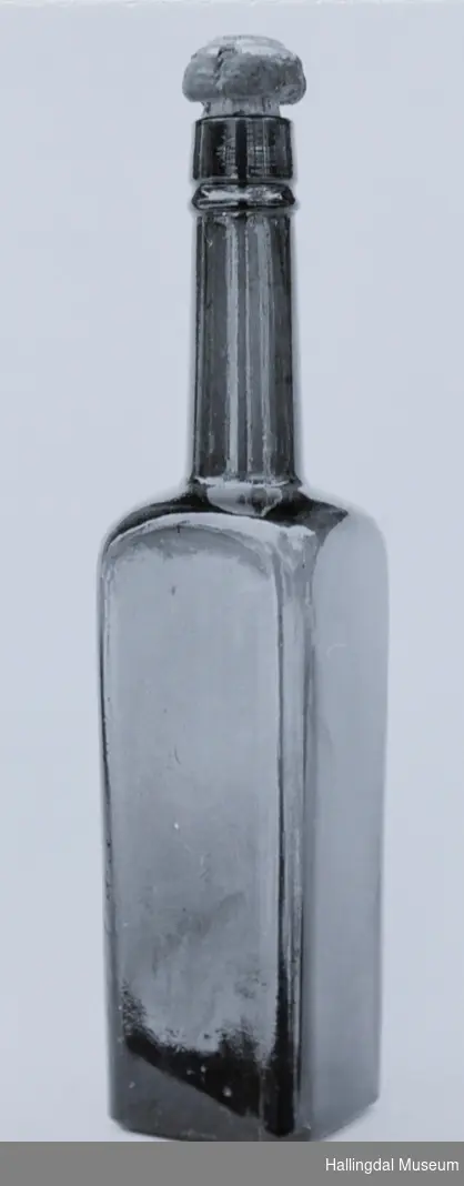 Selve flasken rektangulær med kvadratisk tverrsnitt. Tuten er sylindrisk.
6/6-68. Arne L. Christensen.
