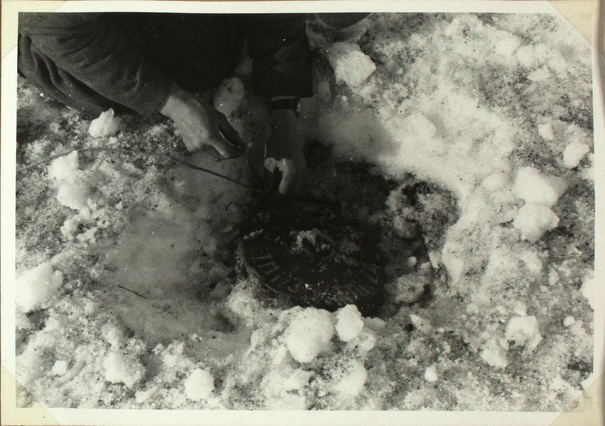 På bildet ser man en tallerkenformet landmine som er gravd ned i snøen. En person graver den ut med blotte hender.