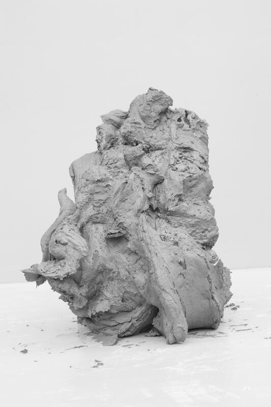 Close-up of a large gray lump of clay on a white table. Photograph.