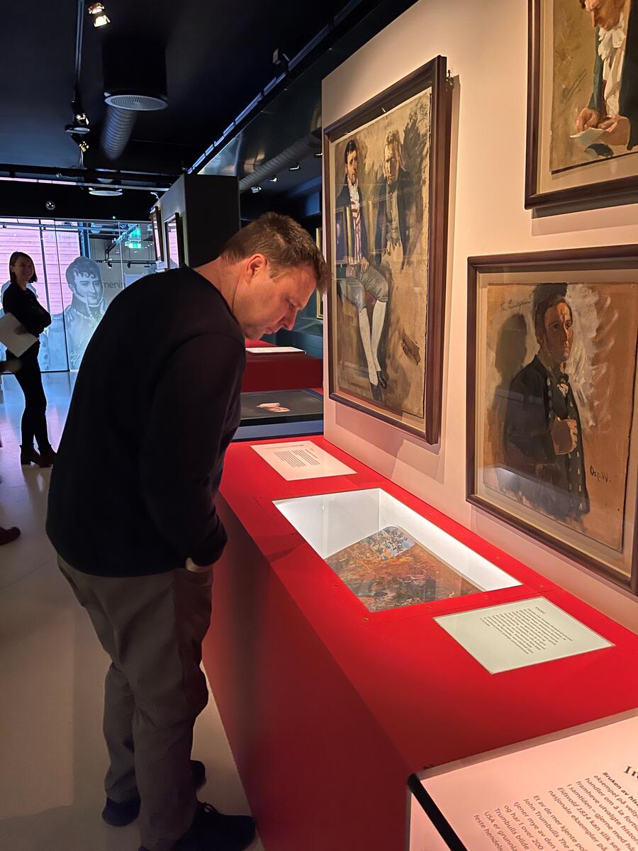Mann ser Oscar Wergelands palett utstilt i en monter. På veggen over henger flere skisser til Wergelands store historiemaleri Eidsvold 1814