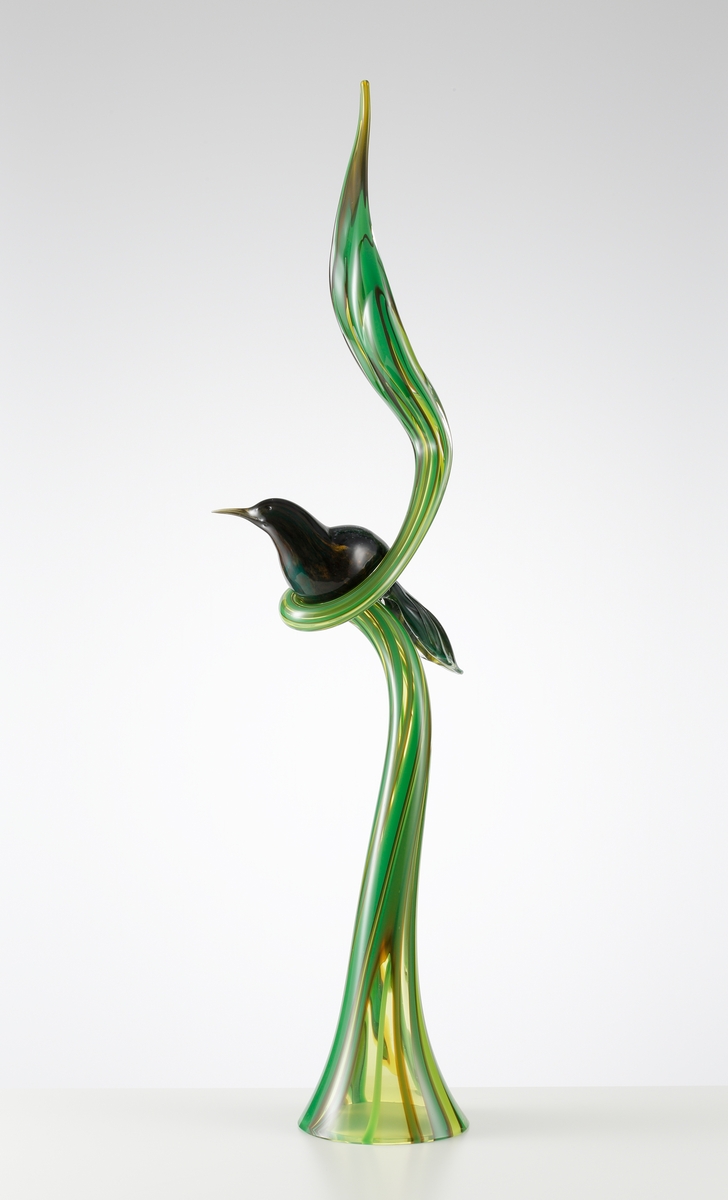 Skulptur bestående av ett en hög grön stående växt som avslutas med ett löv. Växten gör en sväng på mitten, varvid en exotisk, mörk och milerad fågel sitter.