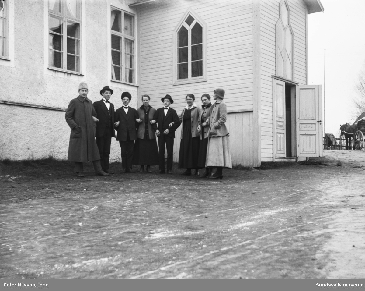 Två versioner av ett gruppfoto med åtta personer på rad framför baptistkapellet i Fanbyn, Stöde. I bildens högerkant syns en hästskjuts med tvåhjulig vagn.