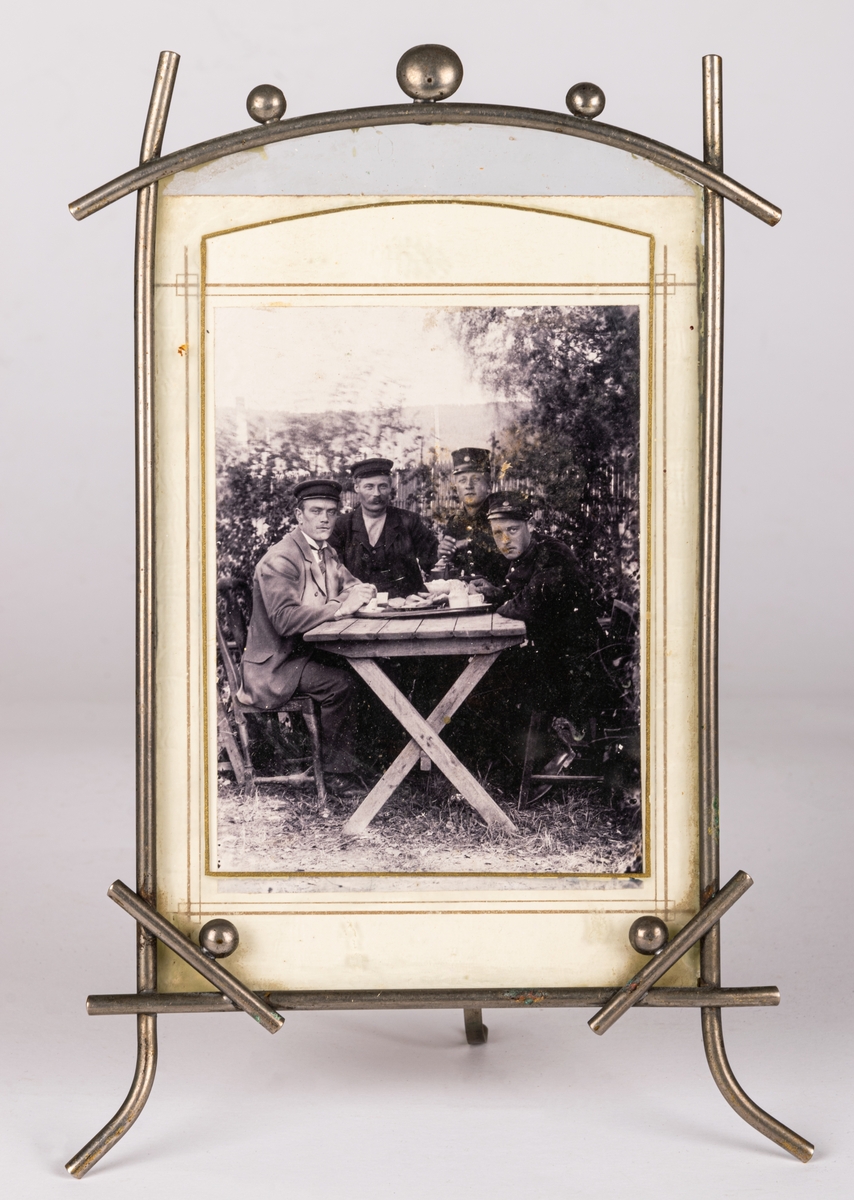 Inramat och glasat fotografi föreställande fyra män vid ett trädgårdsbord. Mannen längst till vänster är Arvid Nordlund. Fotograf Gerda Söderlund, Leksand.