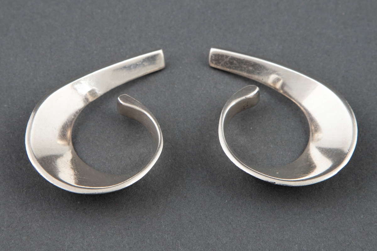 Et par øresmykker, der det ene smykket har form som et 9/6-tall og det andre er speilvendt i forhold til dette. Øresmykkene er laget av mykt avrundede sølvplater som smalner av i hver ende, avrundet i den ene, tvert avsluttet i den andre.