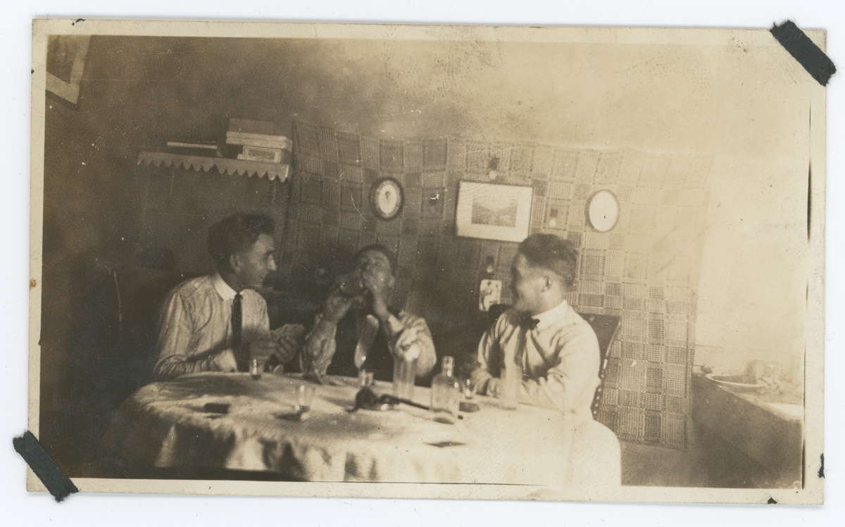 Tre unge menn har innvielsesfest for ny leilighet. De spiller kort og drikker, med snapsglass på bordet.