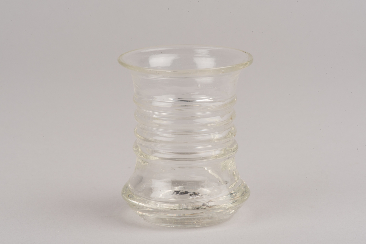 Runt glas med insvängd midja, dekorerad med fyra lodräta vulster runt glasets mitt.
Glastypen kallas länsmansglas eller fyrbandsglas.