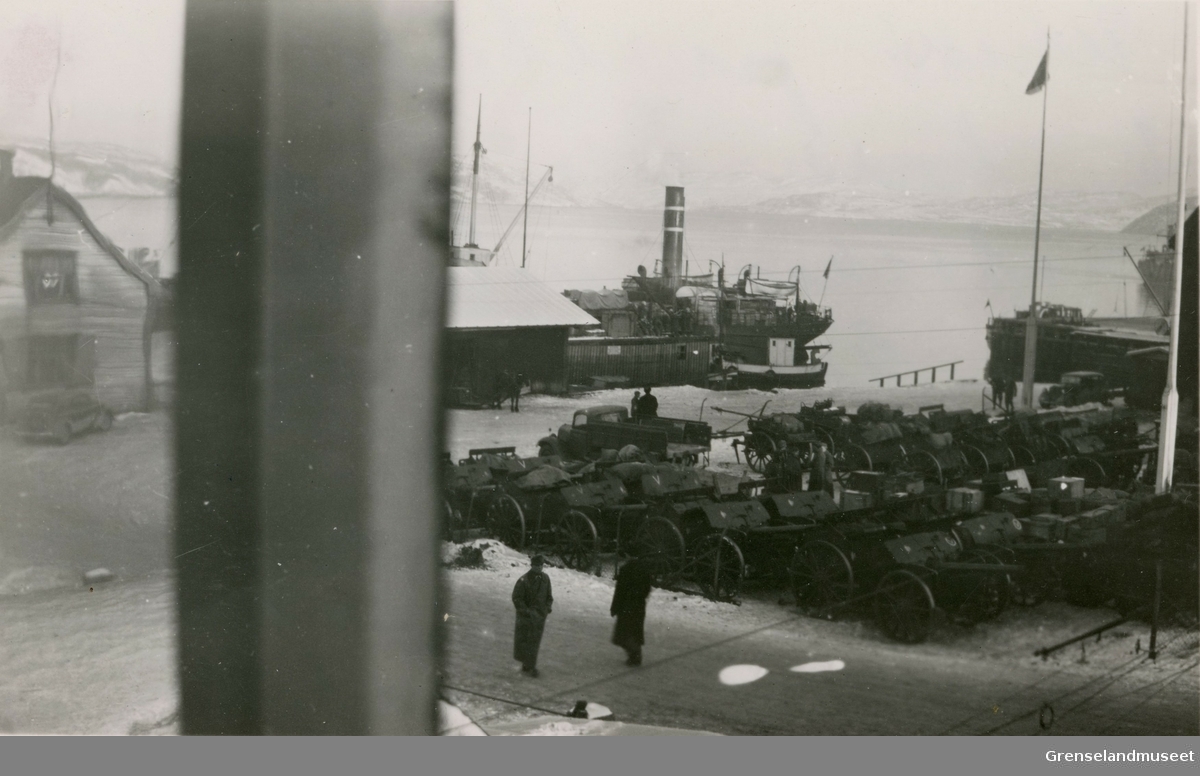 Utsikt fra telegrafstasjonen mot kaien i Kirkenes under krigen i 1941. Nye kanoner står lagret i påvente av videre transport. 