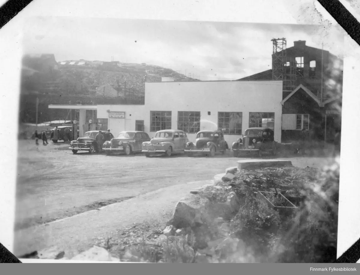 "Bilholdeplassen i Kirkenes, 1947". Stor Shell bensinstasjon i funkisstil. Bilene foran fra venstre: Plymouth 1946-48 drosjeregistrert, mulig Buick 1939-40, Ford 1946, Willys 1937-38, ukjent i typisk 1935-36-stil.