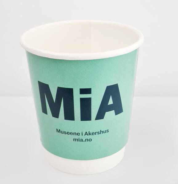 Foto av et pappkrus i mintgrønnfarge med MiA-logo og teksten Museene i Akershus trykket på.