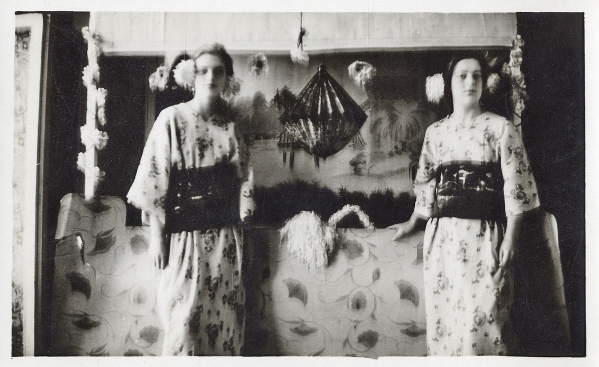 Två utklädda unga kvinnor står vid en öppen spis i ett kök.