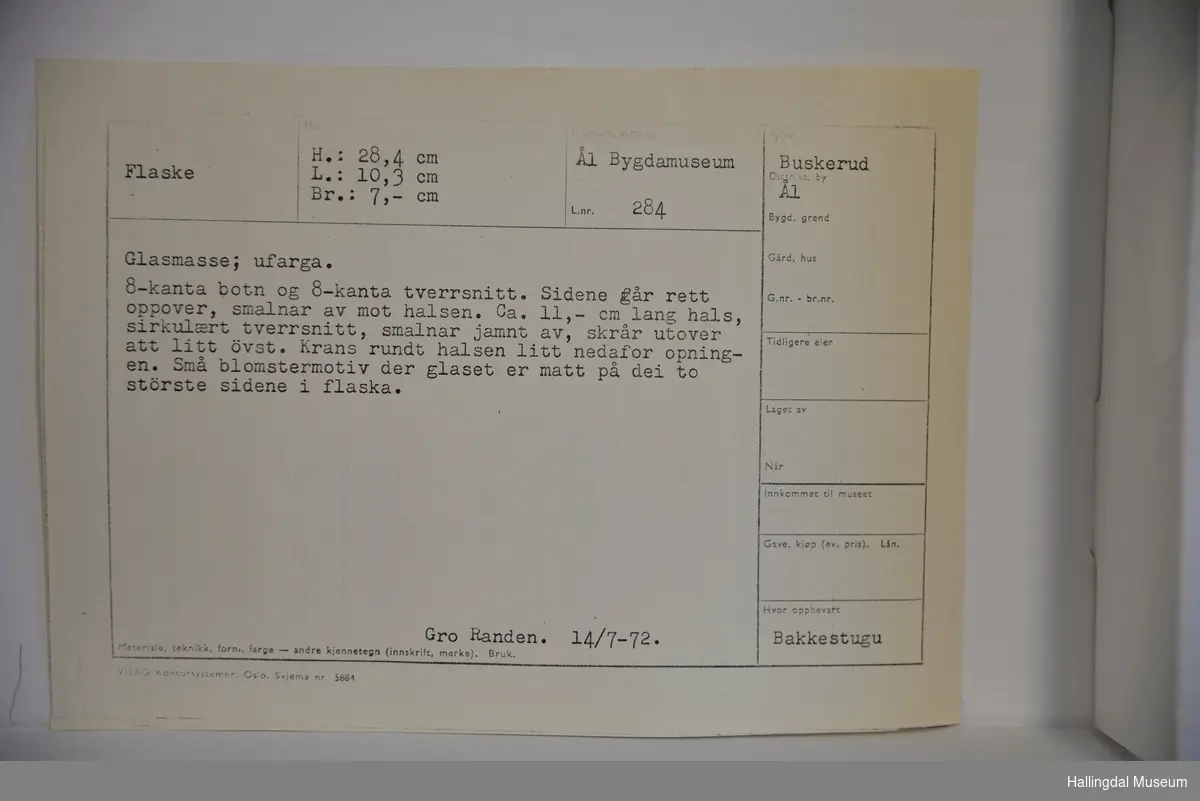 Flaske med 8-kanta botn og 8-kanta tverrsnitt. Sidene går rett oppover, smalnar av mot halsen. Ca. 11 cm lang hals, sirkulært tverrsnitt, smalnar jamnt av, skrår utover att litt øvst. Krans rundt halsen litt nedafor opningen. 