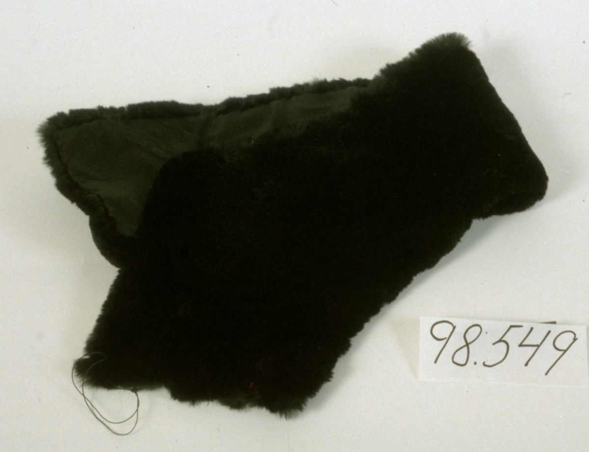 Skinnkrage av svart kaninskinn fodrad med svart silke. På ena kortsidan två stora skinnknappar och på den andra två stora knapphål.