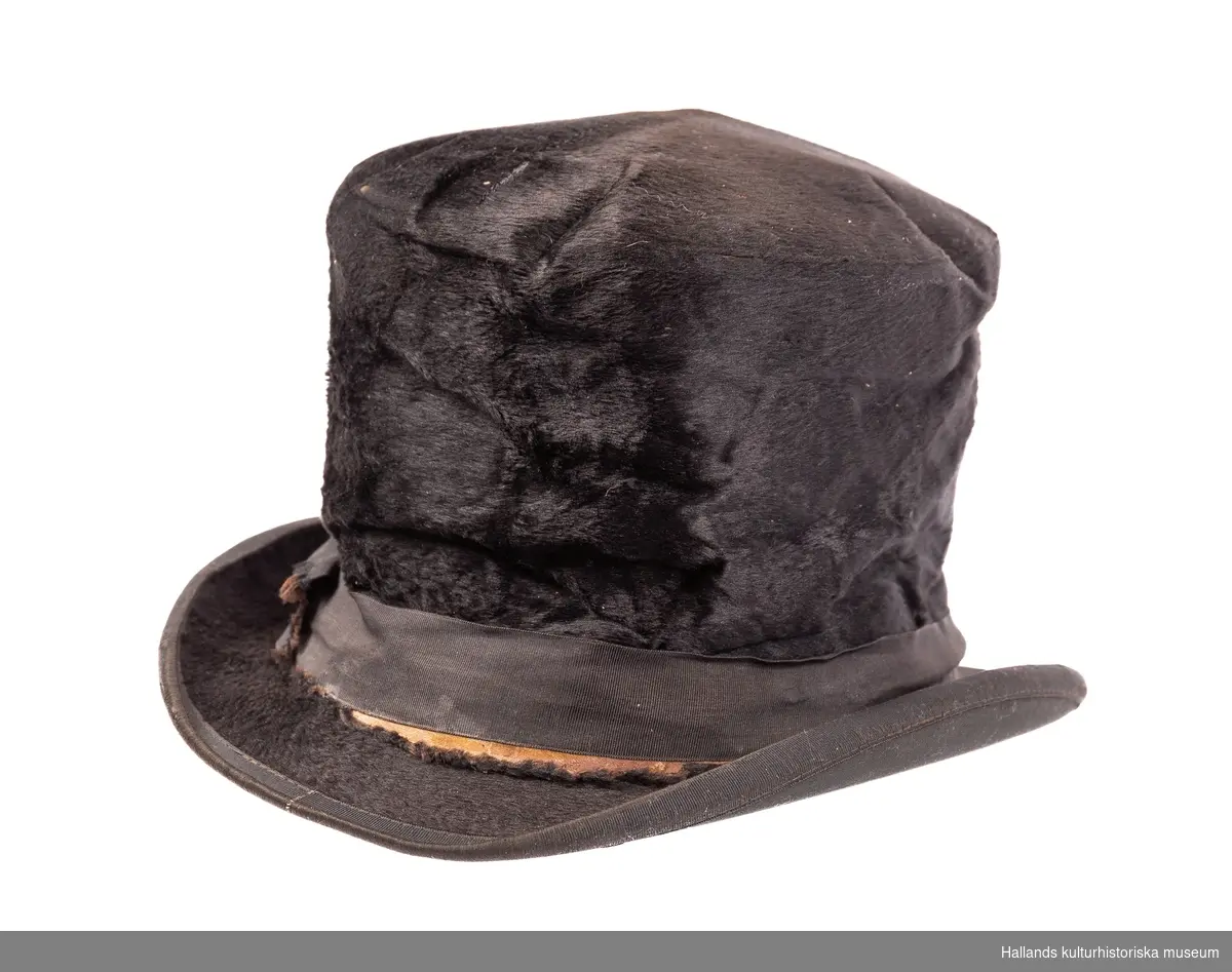 Hög hatt, klädd med svart silkesfilt och kanter med ripsband. Fabriksmärke "Best Quality". Mycket illa medfaren.