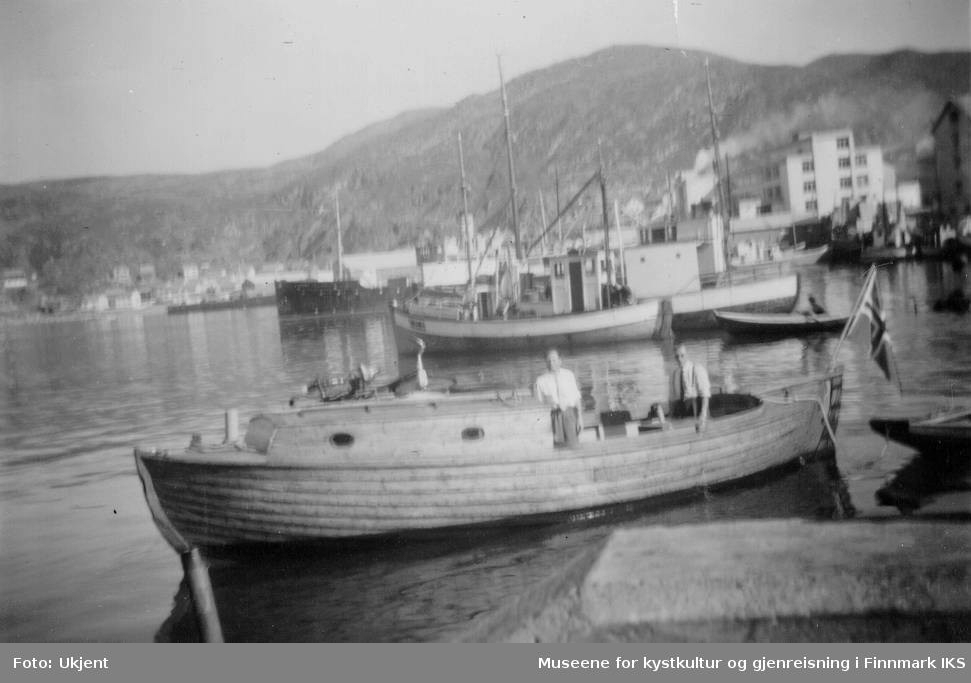 Bildet viser en motorbåt, også kalt for snekka, som legger til ved Nissenkaia i Hammerfest havn, trolig på 1950-tallet. I bakgrunnen ser man at Findus-fabrikken har kommet på plass allerede. På båten står det to menn som ser mot kameraet. I hekket av båten vaier det norskeflagget. I bakgrunn ser man Hammerfest kai og flere andre båter. Båten tilhørte mest sannsynlig familien Normann fra Melkøya.