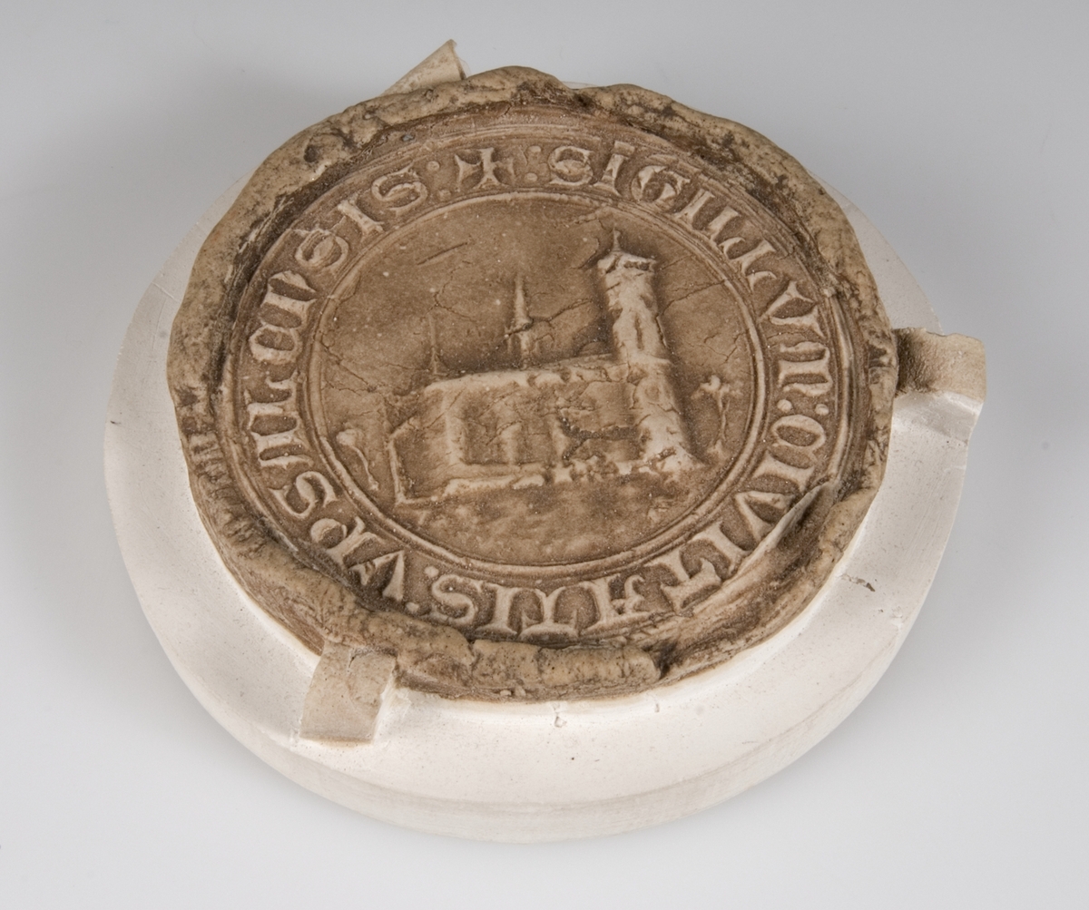 Gipsavtryck av brunfärgad gips på rund gipsplatta av Uppsala stads sigill 1438 19/6 RA perg. Kyrkobyggnad och text "SIGILLUM CIVITATIS UPSALANIS".
