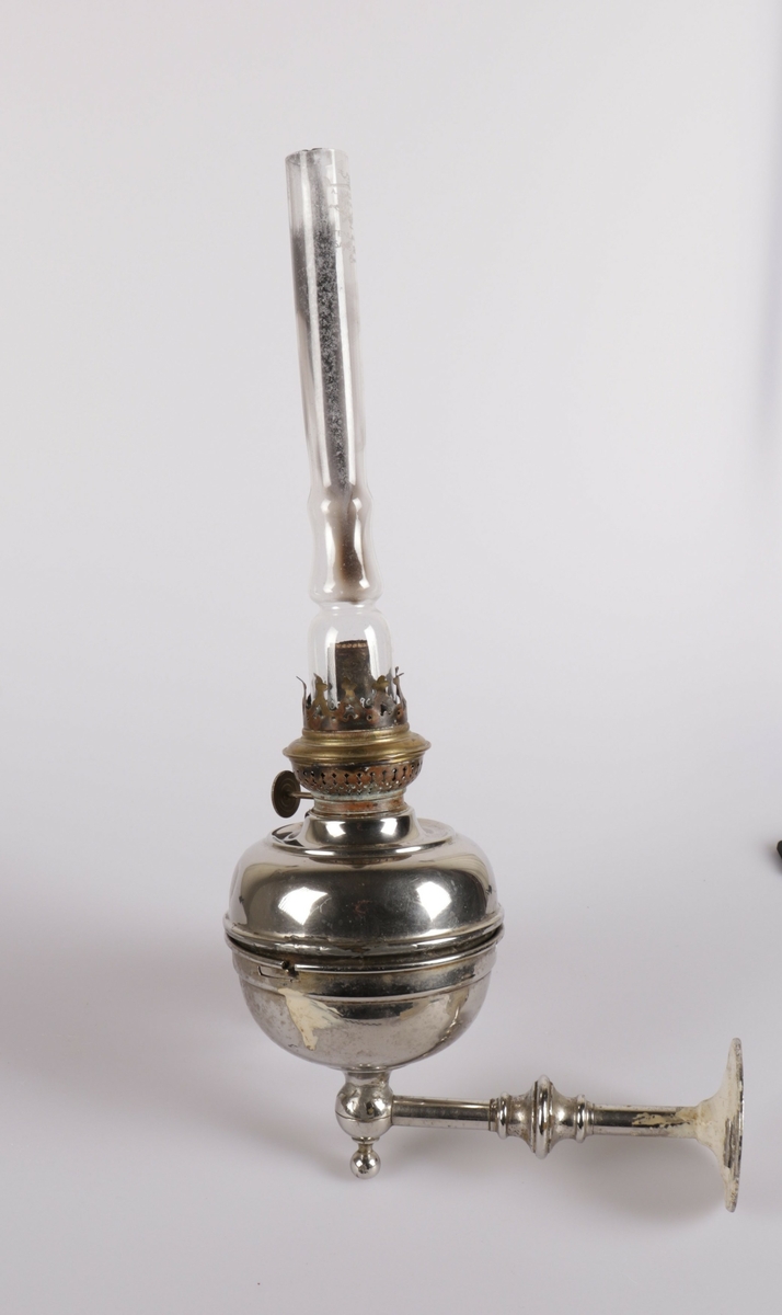 Parafinlampen består av tre deler, veggholder (1) lampe (2) og glass (3). Lampeholderen har to hull i festplaten for å sku den fast til skottet. Det er en  hvit malingsflekk  på siden og på skrufestet. Selve lampen blir skrudd fast til selve holderen. Lampeglasset er sotete og står over veken i kosmosbrenneren. Sølv emaljen er slitt bort enkelte steder.