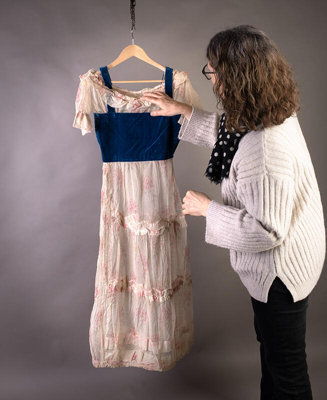 Kvinne som ordner på en kjole fra Norsk utvandrermuseums samling.