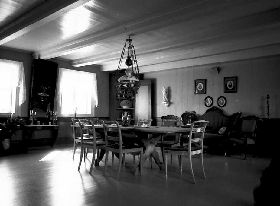 Innvendig i Prestgard, bord, stoler, lampe, sofa. 
