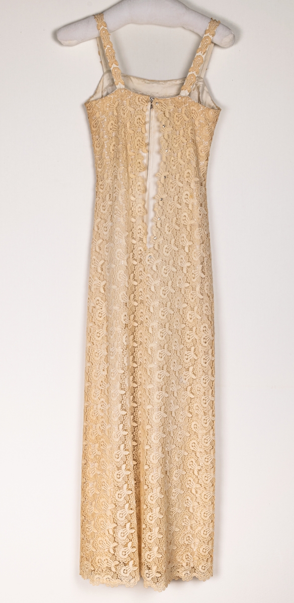 Lång klänning i beige spets med smala axelband. Sydd av Gredèl i Stockholm, troligtvis 1964.
Användes då gåvogivaren, Siv Åberg, tävlade i USA1964.