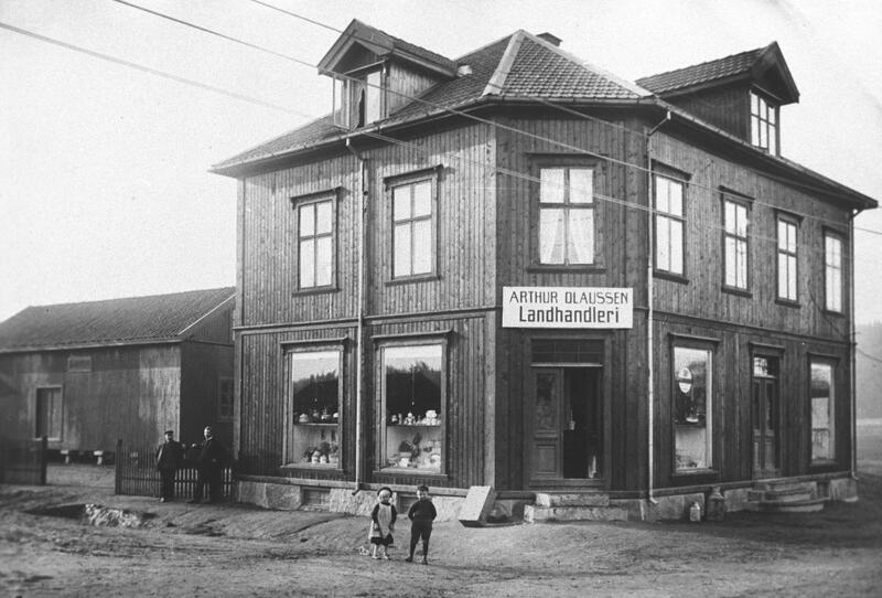 På dette foto av bygningen Aasheim fra 1915 ses Arthurs datter Ruth og sønnen Asbjørn foran landhandelen. Dette var før det ble manufakturbutikk i hjørnedelen av bygningen. På fotoet kan man se en lagerbygning ved siden av landhandelen. Foto: MiA.