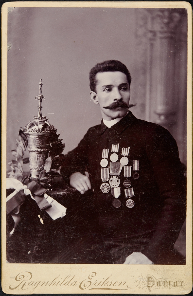 Hamar, HIL, portrett skøyteløper Even Godager, med Stockholmspokalen som han vant 1. mars 1891, pokal og medaljer, innskripsjon på pokalen: "Idrott sterkar sinnet och herdar kroppen"