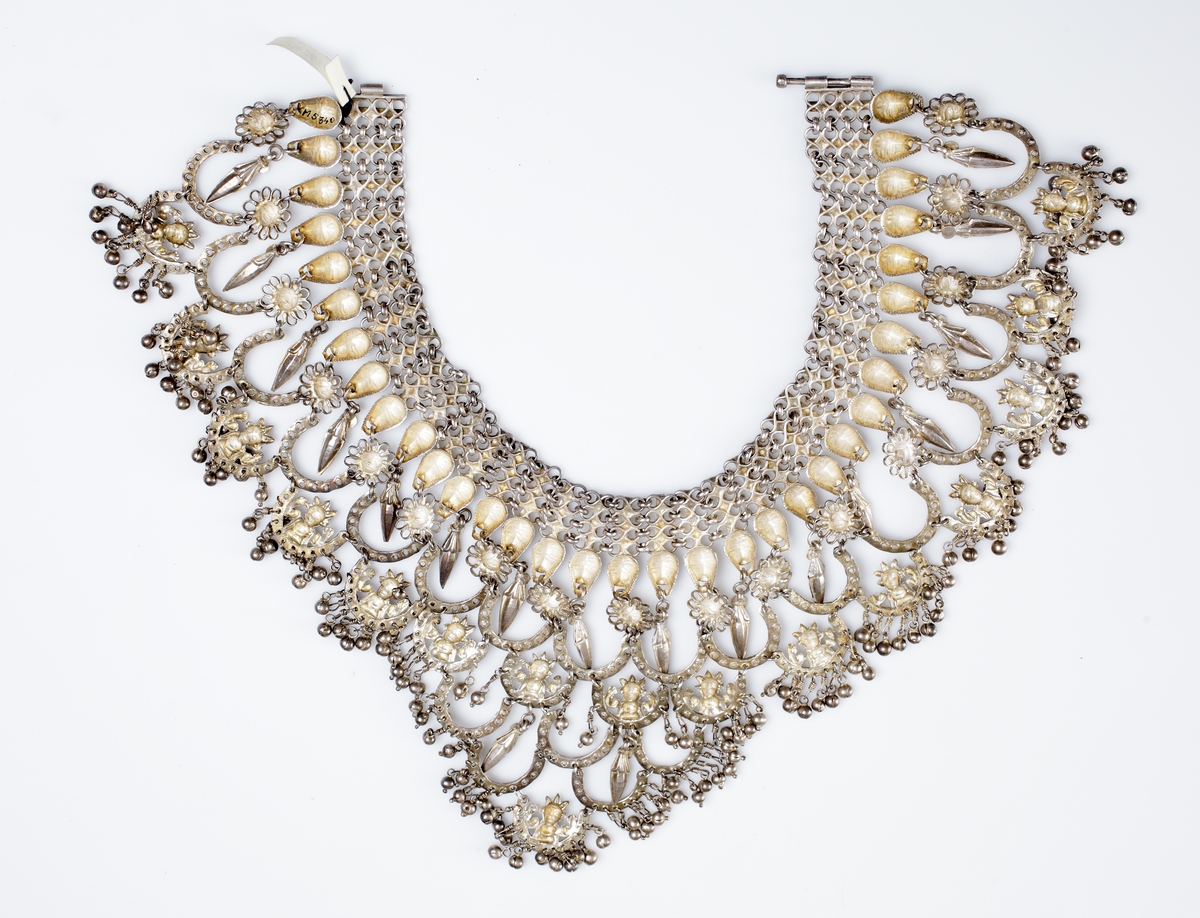 Halsband tillverkat av vitmetall i många sektioner. Det är i form av en halskrage dekorerad med djurhuvuden och olika hästskoformade länkar. 
Har tillhört sångerskan Christina Nilsson de Casa Miranda.

Inskrivet i huvudkatalog 1933.
