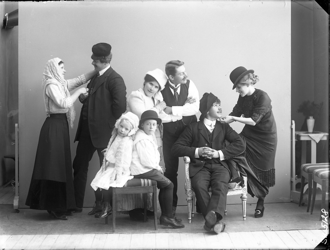 Ett sällskap vuxna, ungdomar och barn som spexar framför fotografen i en ateljé.