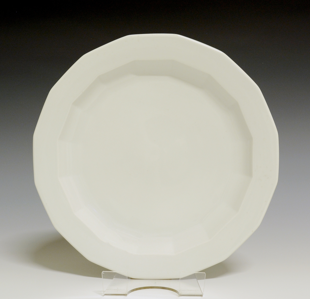 Mangekantet tallerken av porselen med hvit glasur. 
Modell: Octavia, tegnet av Grete Rønning i 1977.

