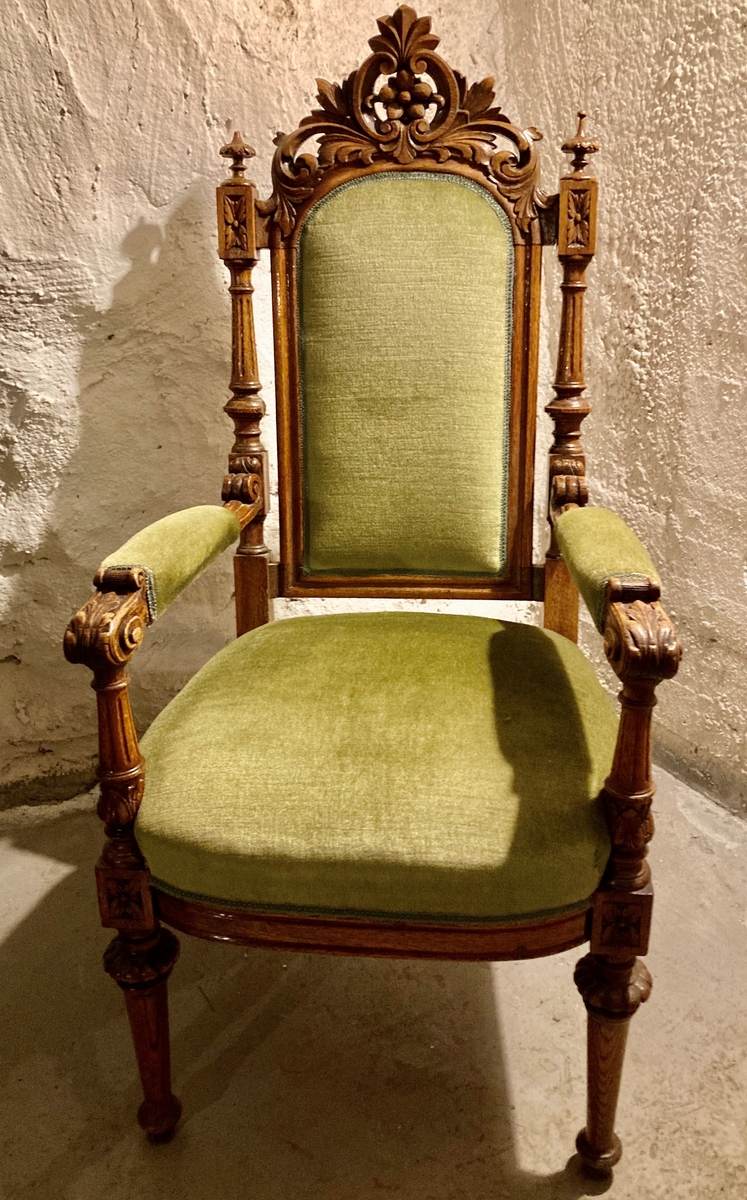 Dommerstol i tre med polstret sete, rygg og armlener, trukket med grønn plysj. Dekorert med utskjæringer med akantus- og blomstermotiv.