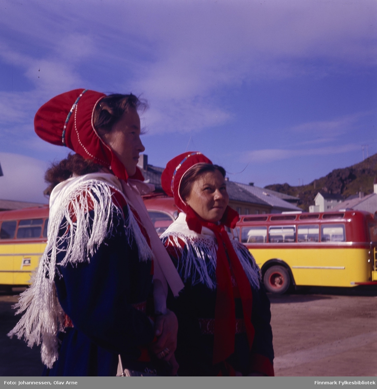 To samiske kvinner i kofte. Bak ser man flere gule og røde busser som var eid av Finnmark Fylkesrederi FFR

Foto trolig tatt på 1960/70-tallet