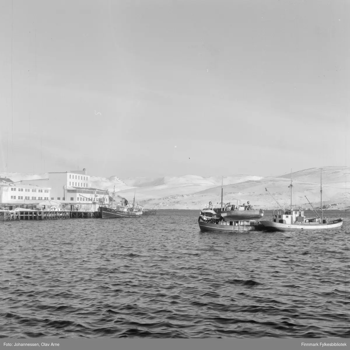 Dampbåt ved gamle DS kai. (til venstre)

Foto av flere fiskeskuter på havet. Til venstre kan man se en kai og bygninger. I bakgrunnen snødekte fjell