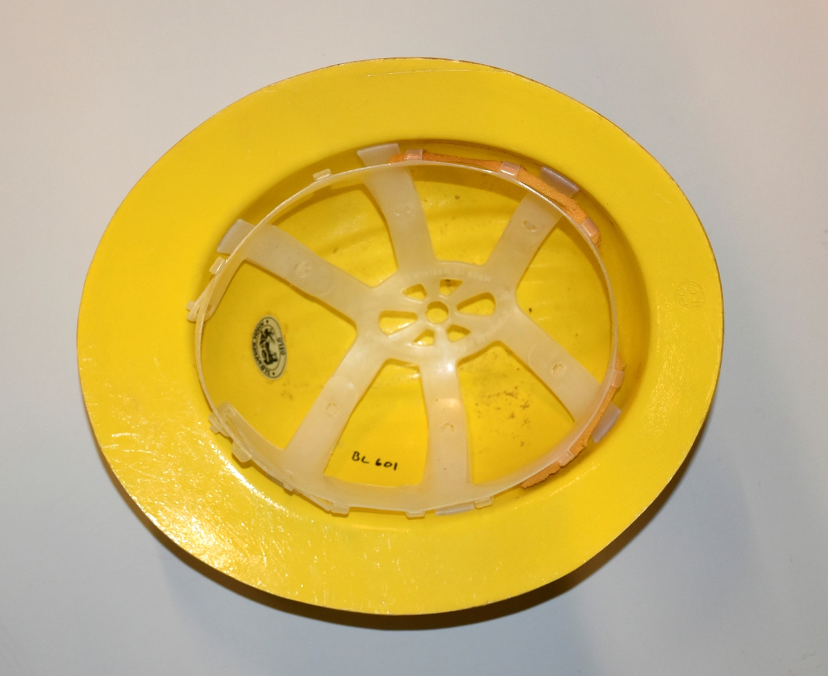 Hjelm i gul plast. Innmaten er laget av plast. Med Industrivern-logo.