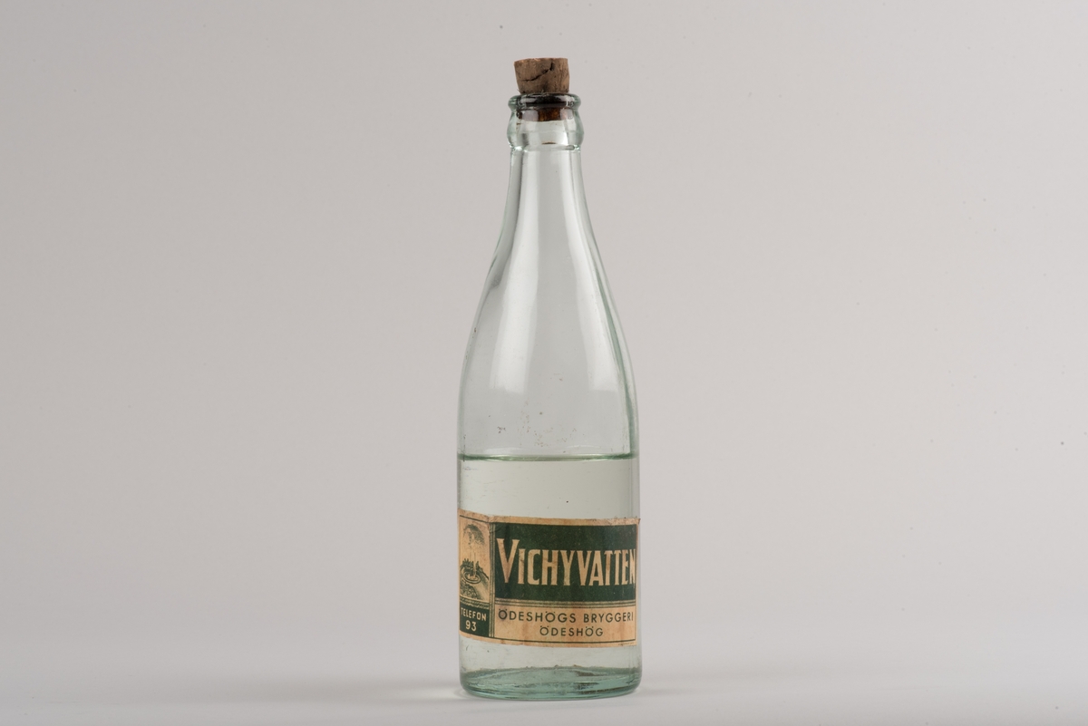 Flaska av klart glas med kork.
Glasflaska med avsmalnande hals. På flaskan finns ett inpräglat L och två stiliserade blommor.
På etiketten framgår det att den tillverkats för vichyvatten i Ödeshög. Numera innehåller flaskan olja.