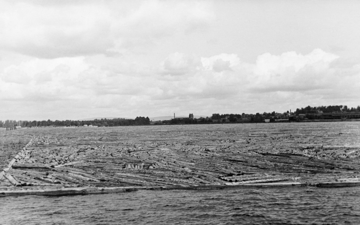 Fra Mora-lensene i det svenske landskapet Dalarna. Her ble fløtingsvirke fra Dalälven samlet og tilsynelatende også sortert med sikte på videre buksering fra Mora i den nordvestre enden av den drøyt 350 kvadratkilometer store innsjøen Siljan til Leksand i sørøst. Dette fotografiet ble tatt i forbindelse med at norske fløtingsfunksjonærer var på befaring i 1935. På dette tidspunktet var det dampbåter som slepte tømmeret over Siljan. Et slep fra Mora til Leksand tok over 30, under ugunstige vindforhold bortimot 40 timer. I 1960-åra ble det innkjøpt dieseldrevne slepebåter som reduserte slepetida til cirka ett døgn. Fløtinga i dette vassdraget ble avviklet ved inngangen til 1970-tallet. Dette fotografiet later til å være tatt ved et tømmersorteringsanlegg med såkalt «kanalsystem», der tømmeret ble ledet inn i innlensete «renner», omgitt av flåteganger, hvor fløterne kunne vandre med fløterhaker og «stikke» stokker med samme kjøpermerke inn i «lommer». Dette fotografiet ser ut til å være fra et flytende tømmermagasin med enorme mengder løstflytende virke. Tømmervolumene i Dalälvfløtinga var størst i begynnelsen av 1950-åra, da det ble ekspedert om lag 10 millioner stokker gjennom Mora lense i løpet av en sesong.
