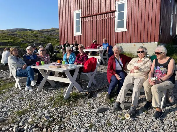 Flere mennesker i solveggen til naustet på Fuglenesodden Friluftsmuseum.