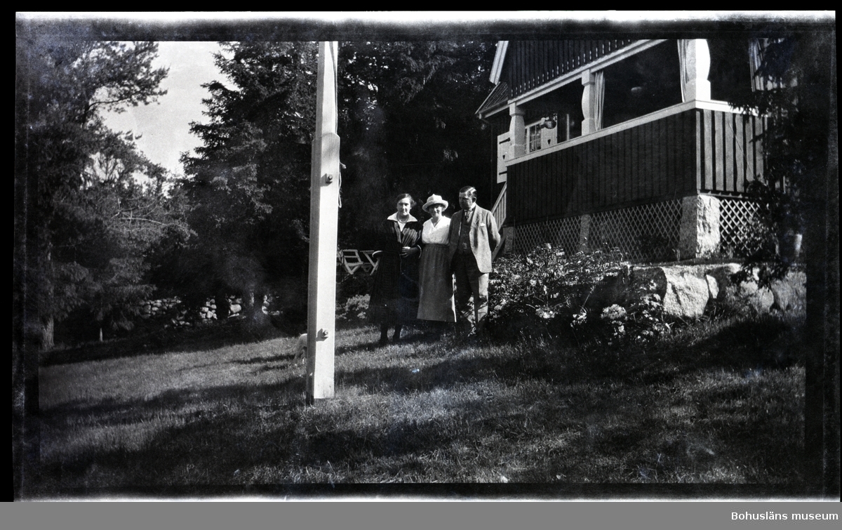 Tre personer framför en veranda i en trädgård.