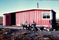 To personer sitter utenfor hytte. Bilde fra Bjørnar Nilsen, 