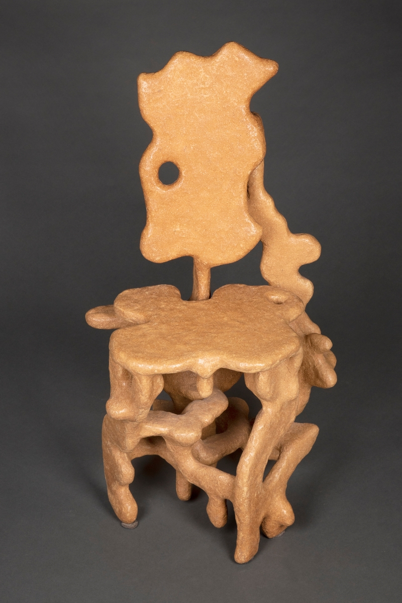Skulpturell stol modulert i en masse laget av trestøv blandet med lim. Organisk formspråk, som om formen har vokst opp naturlig fra skogbunnen. Sitteplate, ryggplate og fem bein, alle deler med avrundede former og myke "utvekster". De negative rommene som oppstår i stolens silhuett blir en del av uttrykket.