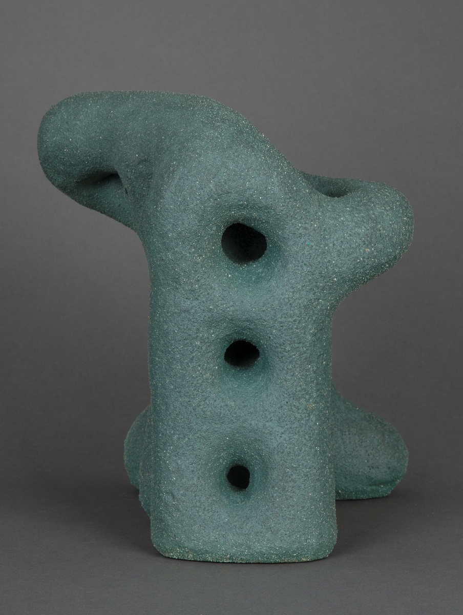 Organisk skulptur i modellert steingods. Blågrønn overflate, grovt og kornete gods. Abstrakt form, med hint til noe figurativt, som et dyr på fire bein.