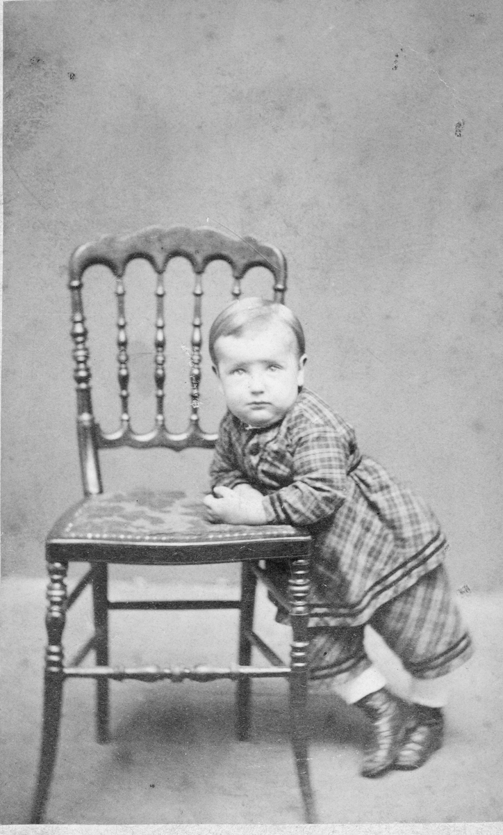 Ur grosshandlare Oscar Nordbloms fotoalbum. Ateljéporträtt av Oscars storebror Gustaf Nordblom, klädd i rutig kolt och byxa, som står och stödjer sig på en stol. Wilhelm Ranch var fotograf i Göteborg innan han etablerade sig i Varberg 1872 och stämpeln på fotografiets baksida anger båda städerna.