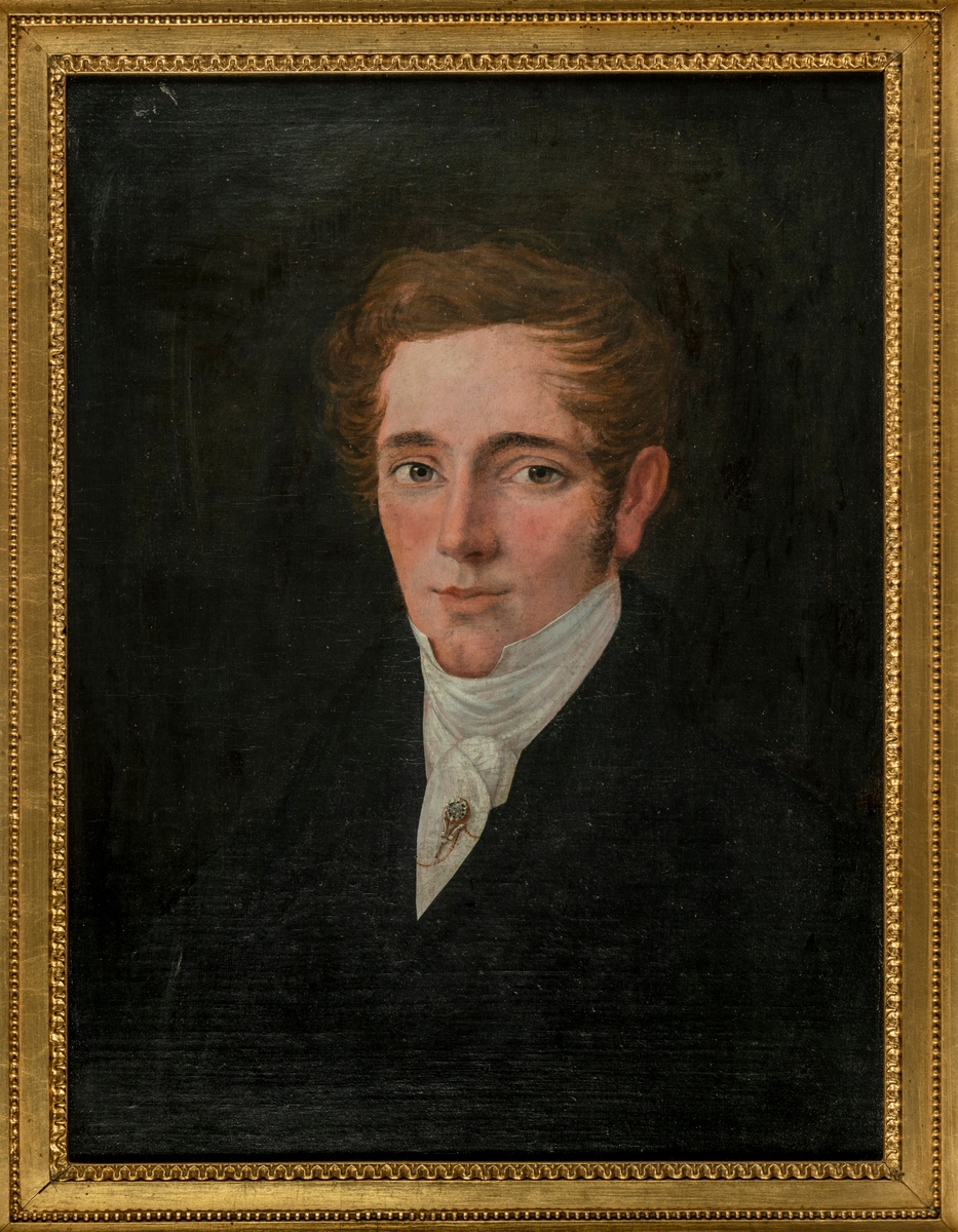 Portrett av ung mann, venstrevendt, foroverbørstet hår, mørk drakt med hvitt halsbind med brosje og lang nål.