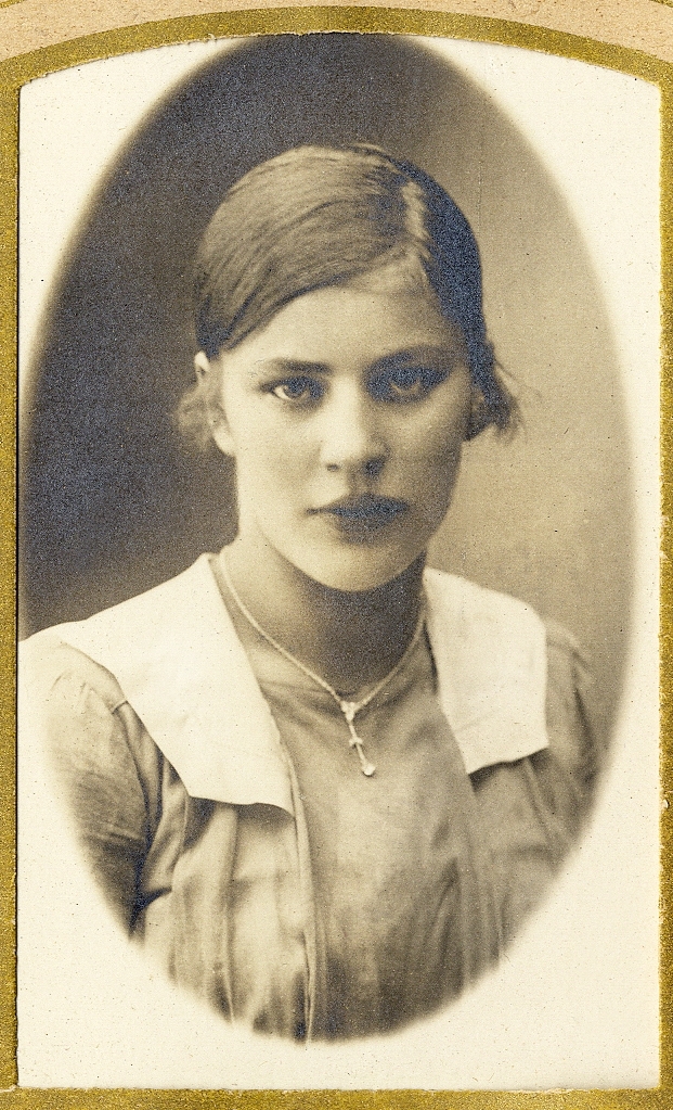 En ung kvinna i klänning med vit krage. Runt halsen syns en halskedja.
Under fotot text med blyerts: "kusin". 
Bröstbild, halvprofil. Ateljéfoto.