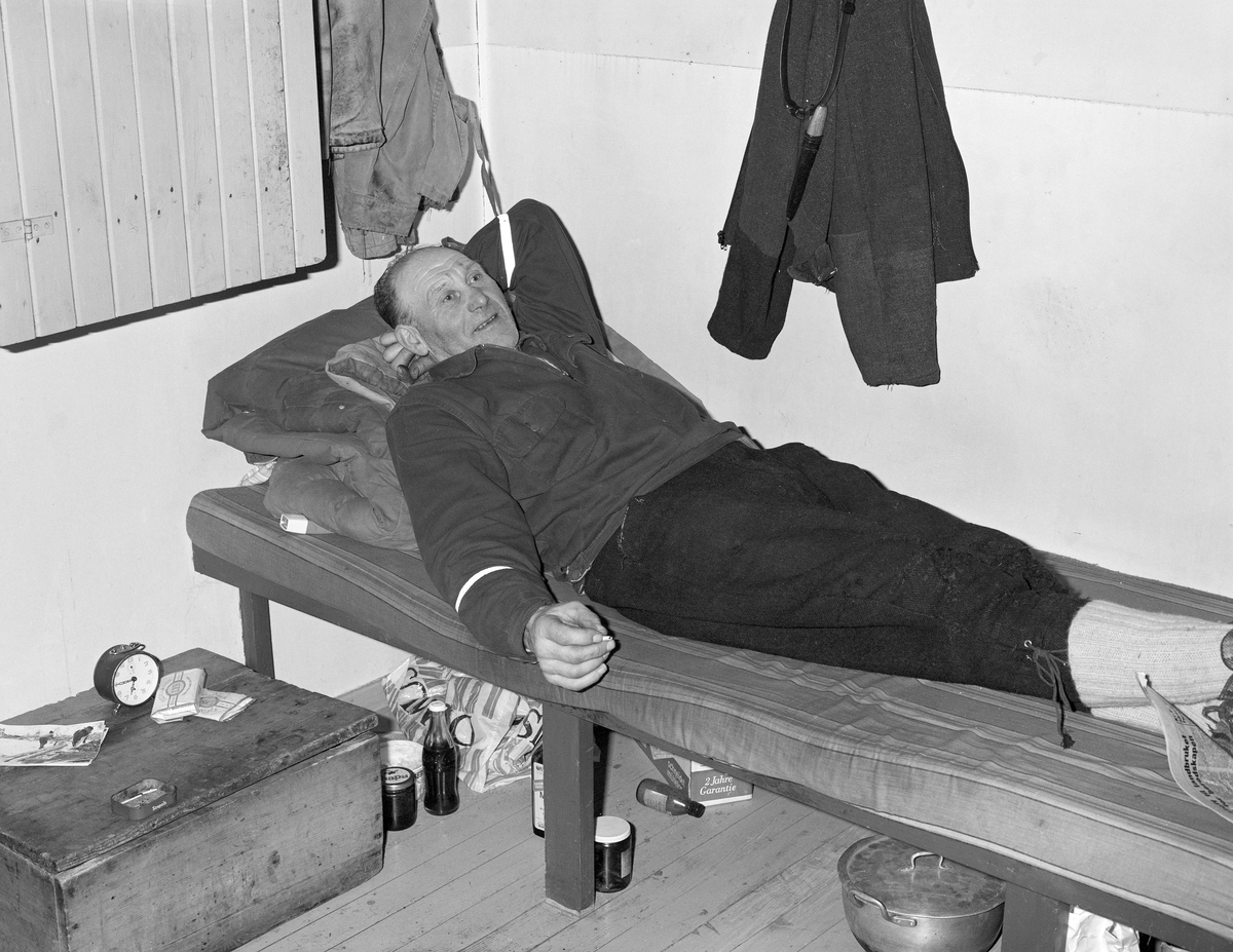 Skogsarbeider hviler i koia. Johan Rasch ligger i senga si i Smaltjernkoia i Svartholtet, Elverum, Hedmark i januar 1975.