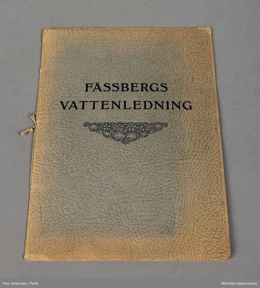 Ett häfte med mjuk pärm som innehåller information om Fässbergs vattenledning. Häftet är i A 4 format och ytan är präglad och har en grå grön nyans. I mitten på framsidan finns rubriken och därunder finns ett emblem.