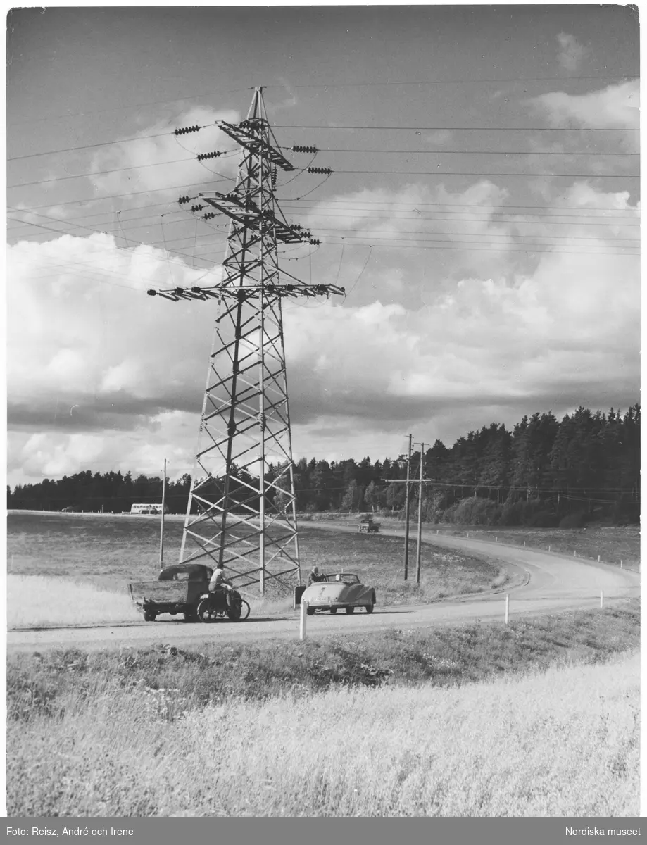 Uppland. Elektrisk kraftledning i Uppland. Bild över en landsväg som slingrar genom lanskapet samt flera olika typer av fordon. En av bilarna har stannat invid vägkanten.